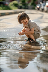 a three-year-old boy is playing in a puddle. Happy children walking outside after the rain on a hot sunny summer day