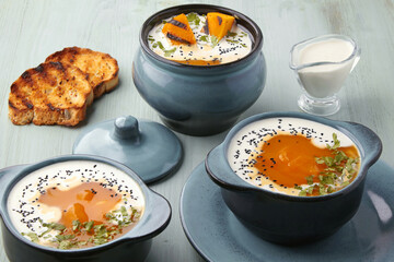 Pumpkin autumn puree soup in a pot and bowl with grilled slices, croutons and milk