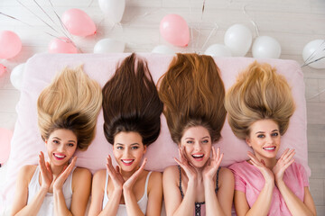 Above view photo of four charming cheerful girl laying linen sheets bed prepare hairdo house indoors