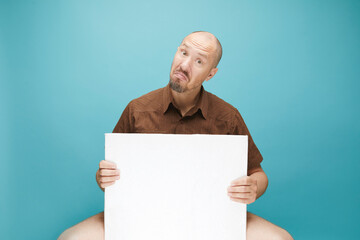  A Bald man with emotion face holding  white board in his hands to fill your text. Isolated on blue background.