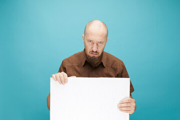  A Bald man with emotion face holding  white board in his hands to fill your text. Isolated on blue background.