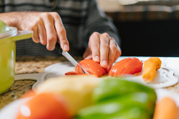 Family kitchen. Close-up of hands holding a knife and cutting tomatoes