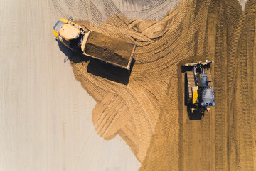 Aerial outdoor view of a tipper truck loaded with a pile of sand and a bulldozer moving the sand making track marks in the sand. High quality photo © PoppyPix