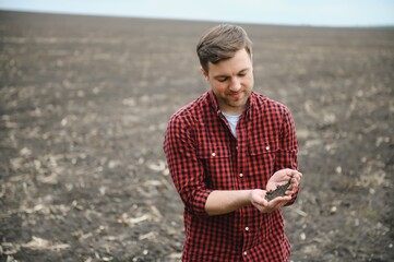 A farmer in boots works with his tablet in a field sown in spring. An agronomist walks the earth,...