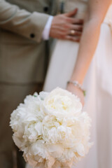 Bride in white wedding dress holding a bouquet of peonies in her hands