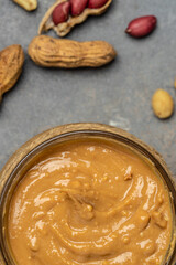 Peanut butter in glass jar and spoon on gray background, American dessert concept. vertical image. top view. place for text