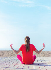 teenage girl sitting on the beach and meditates, back view, copy space. morning exercises, yoga, active lifestyle, health, self-discipline, relaxation and tranquility