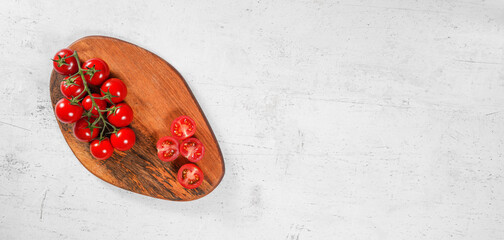 Vibrant small red tomatoes with green vines on wooden chopping board, white stone table under, view from above space for text right side
