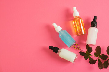 cosmetic serum of different colors for skin care in a transparent dropper bottle on a bright pink background