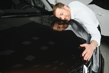 Fototapeta na wymiar Happy handsome bearded man buying a car in dealership, guy hugging hood of new car