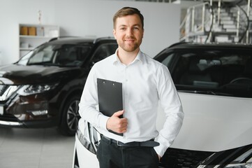 portrait of open-minded professional salesman in cars showroom, caucasian man in white formal shirt...