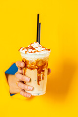 woman's hand holds out a cocktail glass with a coffee drink, frappuccino and ice cubes, with straws...