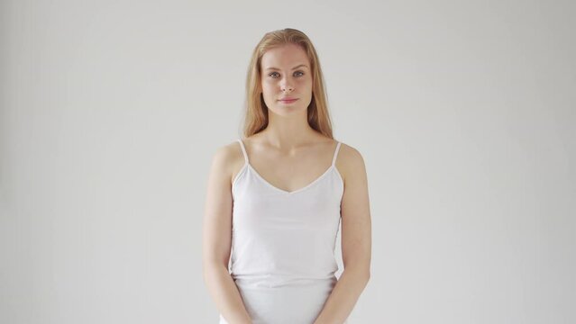 A young beautiful blonde woman stands in front of the camera on a gray background. Portrait of a teenage girl in the studio.