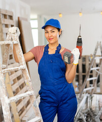 Portrait of smiling asian woman repairer in blue overall. Woman builder with drill.
