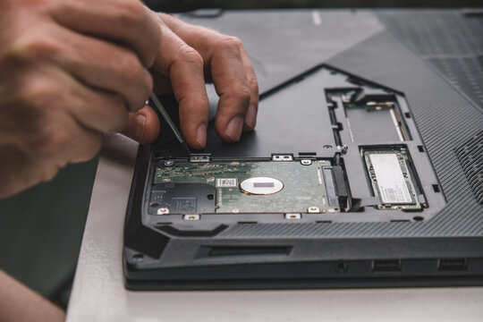 close-up of repairman's hands removing hard drive from laptop case with screwdriver for repair and maintenance. unscrew the screws with a screwdriver. laptop repair and maintenance. selective focus.