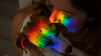 Close-up portrait of a woman hugging a jack russell terrier dog with a ray of rainbow light on her...