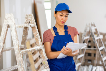 Asian woman worker checking documents during repair works indoors.