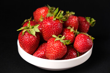 Red fresh strawberries in a white plate on a black background. Summer seasonal berries, close-up