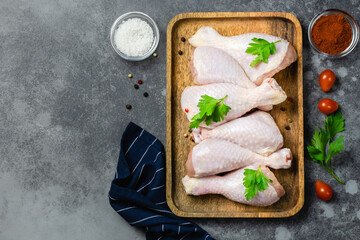 Raw chicken legs with spices and herbs on wooden tray on dark background. Top view, copy space.