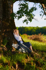 Naklejka premium Young woman posing at sunset by an oak tree