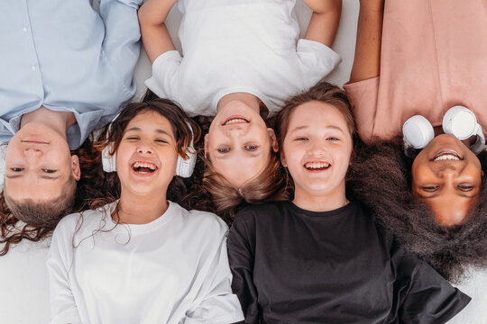 A group of teenagers are lying on the floor looking at the camera and smiling. View from above. The concept of a happy childhood and strong friendship. 