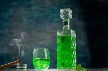 green mint drink in elegant vintage bottle on lighted bar counter with cigar with smoke