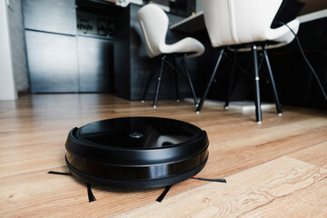 Automatic robot vacuum cleaner in black on wooden floor. New modern technologies for apartment...