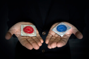 concept of choice. A red and blue condom in a man's hand on a dark background. Safe sex.