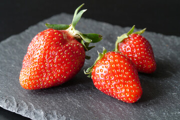 Closeup of three strawberries on a black stone plate