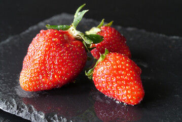 Closeup of three wet strawberries on a black stone plate