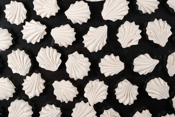 White meringues on a black background, sweet pastries, a dessert of sugar and egg white.
