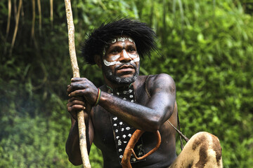 Portrait of Dani Tribe man wearing koteka, traditional clothes of Papua. Dani tribe men looking around and ready to hunt animal prey in the jungle. 