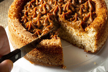 man hand cutting a slice of typical brazilian churros cake with dulce de leche, on a table,...