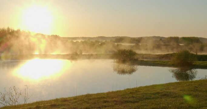 the morning sun over the lake from which comes steam, smoke. a meditative picture for peace of mind. 