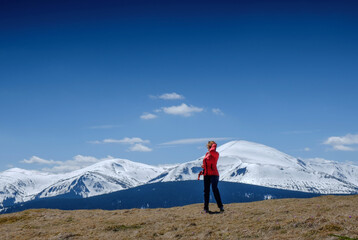 Obraz premium A young girl at the top of the mountain looks at the snowy mountains in the background