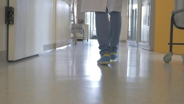 Legs of lab worker in jeans and sneakers walking in lab corridor. Tracking shot.