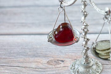 Red heart and silver coins placed on an old-fashioned vintage balance scale on a wooden table. Copy...