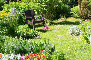 A beautiful blooming flower garden with brown wicker chair on a green lawn in summer. Shallow depth of field
