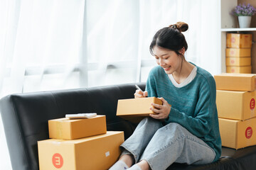 Obraz na płótnie Canvas Happy young asian woman startup small business freelance holding parcel box and computer laptop and sitting on sofa, Online marketing packing box delivery concept.