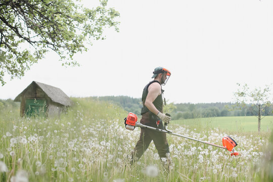 Man mowing tall grass with petrol lawn trimmer in the garden or backyard. Process of lawn trimming with hand mower