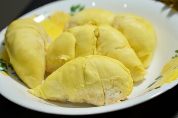 Fresh durian in packaging on white dish with durian peel on banner black  background. Durian king of fruit. Tropical fruit. Topview of ripe durian, wood cutting and rind on table