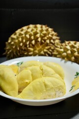 Fresh durian in packaging on white dish with durian peel on banner black  background. Durian king of fruit. Tropical fruit. Topview of ripe durian, wood cutting and rind on table