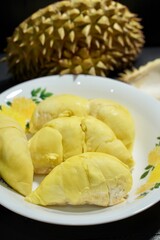 Fresh durian in packaging on white dish with durian peel on banner black  background. Durian king of fruit. Tropical fruit. Topview of ripe durian, wood cutting and rind on table