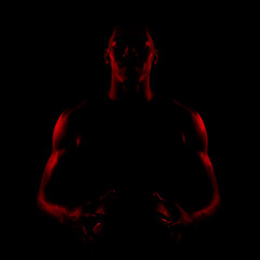 Basketball player side lit with red color holding a ball against black background. Serious...