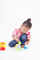 Lovely little cute asian girl playing on the floor with lots of colorful plastic blocks in studio, isolated on white background