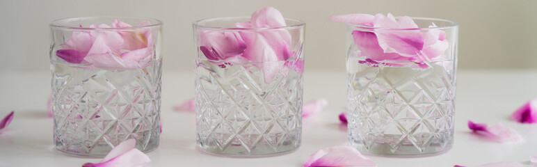 crystal faceted glasses with gin tonic and petals on grey background, banner.