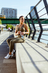 Pretty young woman with earphones takes a break after running in urban area