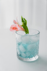 crystal glass with pink alstroemeria flower and iced tonic drink on white background.