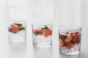 transparent glasses of tonic drink with chopped strawberries on white surface.