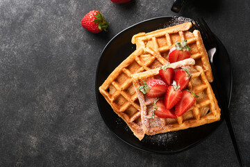 Belgium waffles. Homemade waffles with strawberries, powdered sugar and cup of coffee on black plate on black stone table background. Breakfast. Top view. Mockup for design idea. - obrazy, fototapety, plakaty
